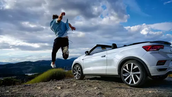 Une Volkswagen T-Roc Cabriolet blanche garée avec un homme sautant à côté d'elle